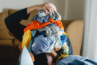 Bir kadın ütülenmemiş bir yığın buruşuk kıyafet tutuyor.