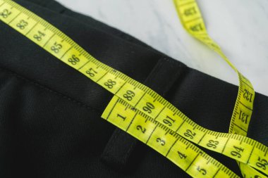 Siyah bir pantolon, sarı bir mezura ile ölçülüyor. Sağlıklı yaşam kavramı