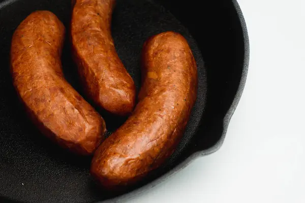 Stock image Frying freshly taken out precook smoked sausages from the chiller using a cast iron skillet