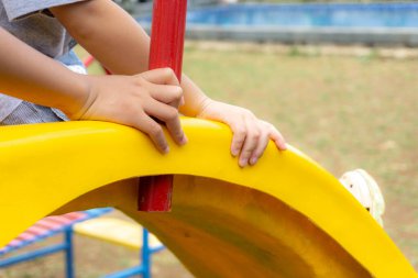 Ağabeyi küçük kardeşiyle oyun parkında oynuyor, sarı kaydırağını tutuyor.