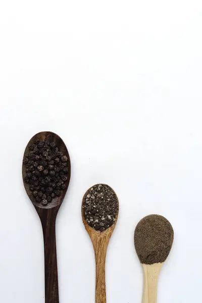 Bütün, kaba ve ince öğütülmüş siyah biber ahşap kaşık üzerinde, beyaz arka planda izole