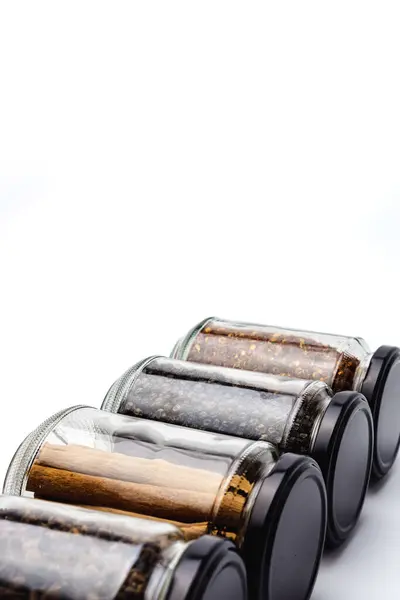 Cam kavanozdaki çeşitli kurutulmuş baharatlar, tarçın, karanfil, karabiber ve hardal tohumları, beyaz arka plandaki mutfak baharatı organizasyonu kavramında izole edilmiş., 