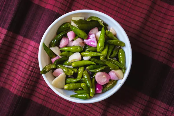 Kırmızı bambu örgülü beyaz bir kasede kırmızı biber, arpacık soğanı ve sarımsak turşusu 