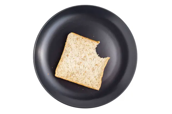 Siyah tabakta bir dilim sade ekmek kısmen yenmiş, beyaz arka planda izole edilmiş.