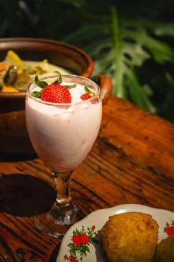 Bir bardak çilekli meyve püresi. Açık havada, ahşap bir masanın tepesinde taze çilekler.