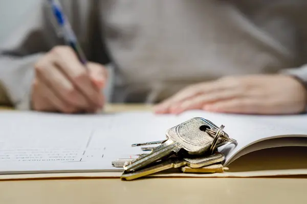 Bir kadın kontörlü ev almak için anlaşma yapıyor. Ön planda yıpranmış bir ikinci el anahtar. İkinci el mülk alma kavramı.