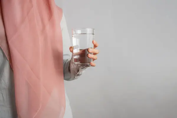 Şeftali rengi tesettürlü Müslüman kadın ya da bir bardak su tutan kafa scraft, sağlıklı yaşam tarzı kavramı, gri arka plan