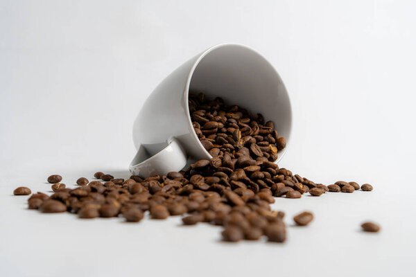 arabica roasted coffee bean's spill from a white mug, isolated on white background