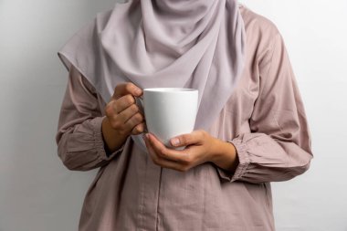 Beyaz bir kupa tutan Müslüman kadın, beyaz arka planda izole edilmiş.