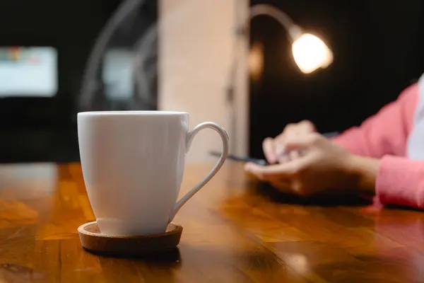 Bir kupa sade kahve ve elinde tablet olan bir kadın akşamları fazla mesai yapıyor.