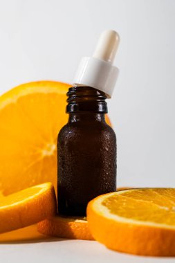 Kahverengi kehribar cam yüz serumu veya yağ şişesi, arka planda portakal dilimleri yığını, temel yağ özü kavramı, beyaz arka planda izole