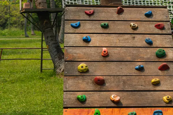 Yapay tırmanma duvarı çocukların oyun alanındaki ahşap renkli el tutuşları ya da tutacakları ile yapılmış.