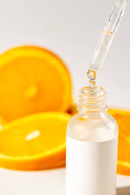 Bir pipetten şişeye damlayan serum yağı, arka planda portakal dilimleri, sağlık ve güzellik kozmetikleri, beyaz üzerine izole edilmiş.