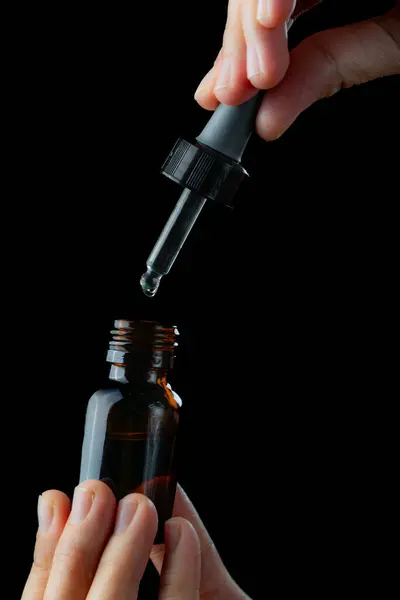 Elinde damlatıcı olan serum uygulanıyor, siyah arkaplanda izole edilmiş.