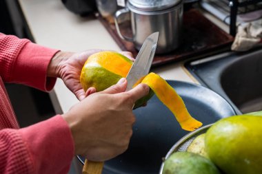 Mutfakta keskin bir bıçakla olgun ve sulu mango meyvesi soyan bir kadın.