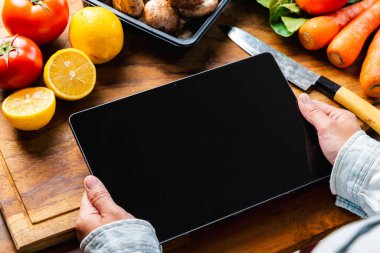 Bir kadın tablet üzerinde yemek tarifi ararken tahta kesme tahtasında taze sebzeler hazırlıyor. Sağlıklı gıda kavramı.