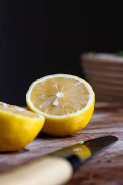Tahta kesme tahtasıyla ikiye bölünmüş taze limon ve yakınlarda bir bıçak, koyu arka plan.