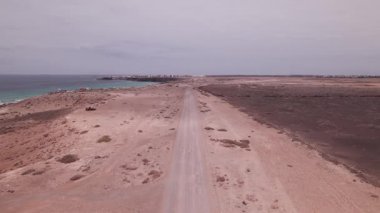 İHA görüntüleri, Fuerteventura 'nın kuzeybatı kıyısında, El Cotillo yakınlarında kızıl çöl toprağı ile çevrili dolambaçlı bir sahil yolunun üzerinde uçuyor. Çorak, volkanik manzara, uzaktaki derin mavi okyanusla çelişiyor..