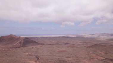 Calderon Hondo volkanı yakınlarındaki çorak, kırmızımsı arazinin üzerinde uçan hava görüntüleri. Çöl benzeri arazide lav lekeli tepeler, toprak yollar ve kuzey Fuerteventura 'da geniş bir açık alan bulunur..