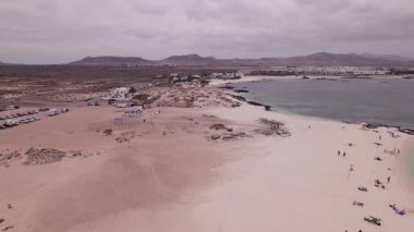 Fuerteventura 'daki La Concha Sahili' nin kıyısından geçen hava geçidi dalgaların kayalık ve kumlu kıyılarla nazikçe buluştuğunu gösteriyor. Güneşin altında sakin, doğal bir sahne.