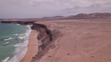 Playa de la Escalera 'nın üzerinde uçan yüksek çözünürlüklü drone görüntüleri kırmızı volkanik kayalıklar ve çöl benzeri kıyı şeridi. Fuerteventura 'daki bu kıyı şeridi, rüzgar ve zamanın şekillendirdiği doğal güzelliği ortaya çıkarıyor..