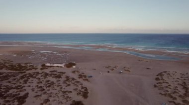 Gün batımında Playa de Sotavento de Jandia ve Risco del Paso 'daki gelgit gölünün insansız hava aracı görüntüsü. Açığa çıkan deniz yatağı ve durgun su, solan güneşin altında doğal desenler oluşturuyor.. 