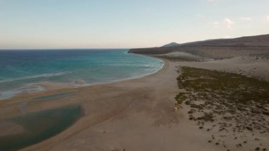 Playa de Sotavento ve Risco del Paso bölgesinin alçak gelgit sırasında çekilmiş yüksek çözünürlüklü bir videosu. Canlı gökyüzü ve açığa çıkan kum desenleri Fuerteventura 'da dramatik bir kıyı sahnesi oluşturuyor.. 
