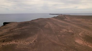 Jandia yakınlarındaki ıssız volkanik ovaların üzerinde uçan İHA, Punta de Jandia deniz fenerine giden dolambaçlı yolu yakalar. Açık gökyüzünün altında engin bir manzara. 