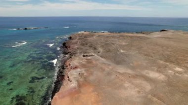 Volkanik kayalıkların Faro de Jandia bölgesi yakınlarındaki parlak mavi Atlantik Okyanusu 'yla buluşmasını gösteren insansız hava aracı görüntüleri. Bu çekim Kanarya Adaları 'nın doğal simetrisini, canlı kontrastını ve vahşi kıyı şeritlerini vurgular..