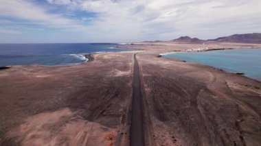 Faro de Jandia 'dan uzaklaşan engebeli çöl yolu boyunca volkanik toprak ve yaban kayalıklarıyla çevrili İHA görüntüleri. Uzak yolculuğun, minimalizmin ve güney noktasının dokunulmamış doğasının güçlü bir temsili.