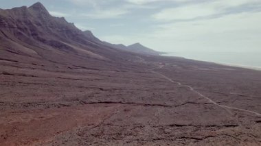 Havadan bakıldığında, beyaz-sarı kumlu kumlu plajdan kuru çöl arazisine ve Fuerteventura volkanik oluşumlarına geçiş..