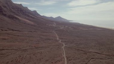 Fuerteventura 'daki Playa de Coffee sahil şeridinin çarpıcı hava görüntüleri, engebeli uçurumlar, turkuaz okyanus ve volkanik tepelerin altındaki geniş kumsal..