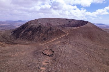 Fuerteventura 'daki Calderon Hondo volkanının insansız hava aracı fotoğrafı. Dramatik dairesel krater ve engebeli volkanik manzara adanın ikonik özellikleridir..