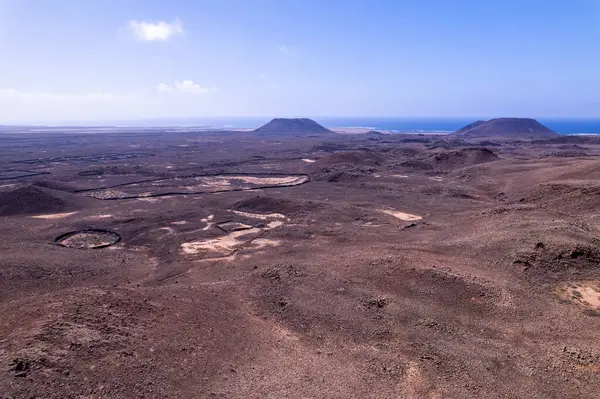Fuerteventura 'nın kırmızı volkanik arazisindeki dolambaçlı toprak bir yolun drone görüntüsü. Çerçevenin hakimi engebeli manzara ve uzak kuru tepeler..