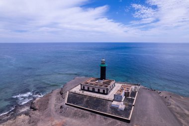 Faro de Jandia deniz fenerinin Atlantik Okyanusu 'na bakan dramatik bir kaya çıkıntısı üzerindeki detaylı görüntüsü. Yapı, berrak mavi gökyüzü ve turkuaz sulara karşı bir işaret feneri olarak duruyor..
