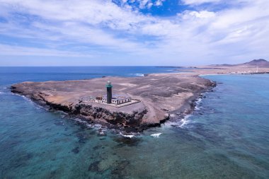 Geniş açılı çekim, Faro de Jandia deniz fenerinin nefes kesici manzarasını ve engebeli çevresini yakalıyor. Görüntü volkanik arazinin, turkuaz suların katıksız güzelliğini gösteriyor. Bu da onu doğa ve manzara fotoğrafçılığı için ideal kılıyor..