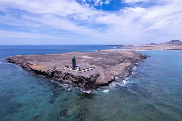 Geniş açılı çekim, Faro de Jandia deniz fenerinin nefes kesici manzarasını ve engebeli çevresini yakalıyor. Görüntü volkanik arazinin, turkuaz suların katıksız güzelliğini gösteriyor. Bu da onu doğa ve manzara fotoğrafçılığı için ideal kılıyor..
