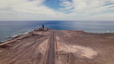 Hava aracı, Fuerteventura 'nın güney ucundaki Faro de Jandia deniz fenerine giden bir çöl yolunu izliyor. Kırmızı toprak, kuru manzara ve uzak okyanus ufku seyahat için ideal bir sinema sahnesi yaratır..