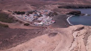 Fuerteventura 'daki Ajuy Mağaraları yakınlarındaki küçük sevimli köyü gösteren detaylı hava görüntüleri. Resimde renkli evler, siyah kumlu plajlar ve engebeli uçurumlar, emlak, seyahat ve yaşam tarzı fotoğrafçılığı için mükemmel.. 