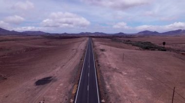 Dinamik hava çekimi Fuerteventura 'daki uzak ufka doğru uzanan düz bir yol gösteriyor. Görüntü Kanarya Adaları 'nın saf güzelliğini yansıtıyor. Seyahat, doğa ve macera içeriği için ideal.. 