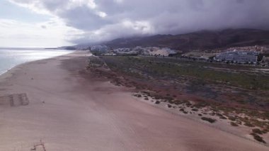 Muhteşem hava görüntüleri muhteşem Morro Jable plajını ve Fuerteventura 'daki canlı kasabasını yakalıyor. Resim, seyahat fotoğrafçılığı için mükemmel olan dramatik bulutlu gökyüzü altında altın kumlar, modern mimari ve yuvarlanan tepeleri sergiliyor.. 
