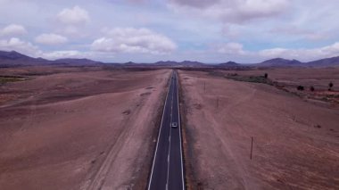 Fuerteventura 'nın uçsuz bucaksız, çorak arazisini keserek düz bir yol yakalayan muhteşem hava görüntüleri. Görüntü, kırmızı toprağın, dağınık bitki örtüsünün ve uzak dağların, seyahat ve doğa fotoğrafçılığı için mükemmel güzelliklerini sergiliyor. 