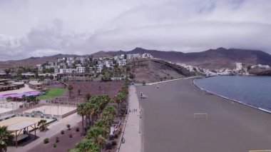 Dinamik hava çekimi Fuerteventura 'daki Playitas' taki siyah kumlu sahili gösteriyor. Görüntü, karanlık kum ve canlı turkuaz sular arasındaki kontrastı yakalar ve onu seyahat, doğa ve yaşam tarzı fotoğrafçılığı için ideal kılar.. 