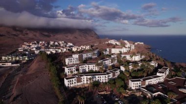 Fuerteventura 'da sahile yakın bir yamaçtaki büyüleyici beyaz evleri çeken muhteşem hava görüntüleri. Görüntü modern mimari, yemyeşil ve turkuaz suların karışımını gösteriyor. Fotoğrafçılık için mükemmel.. 