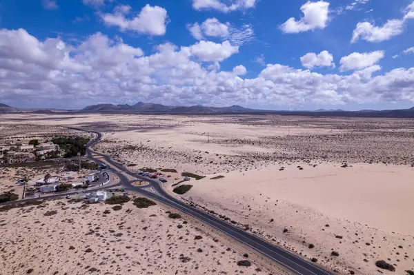 Dinamik hava görüntüleri, Fuerteventura 'daki Corralejo' nun engin çöl manzarasını kesen dolambaçlı bir yolu gösteriyor. Görüntü, kızıl toprağın, dağınık bitki örtüsünün ve uzak dağların saf güzelliğini yakalar.. 
