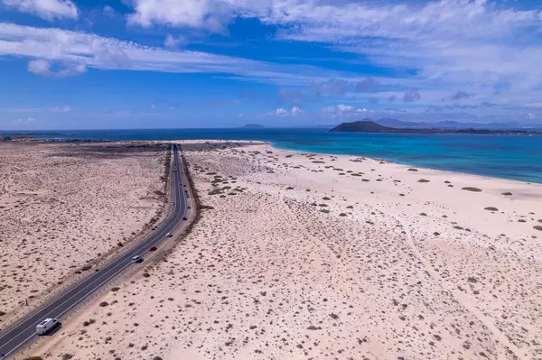 Detaylı hava görüntüleri Corralejo, Fuerteventura 'da okyanus kenarında bir viraj yolu yakalıyor. Görüntü, turkuaz suların yapılandırılmış yolu ile doğal güzelliği arasındaki zıtlığı vurguluyor. Bu da onu seyahat ve yaşam tarzı içeriği için ideal yapıyor..
