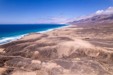 Muhteşem hava manzarası Fuerteventura 'daki Playa de Cofete' de Roque del Moro yakınlarında geniş bir sahili yakalıyor. Görüntü, seyahat fotoğrafçılığı için altın kumlar, turkuaz sular ve engebeli arazi arasındaki zıtlığı gösteriyor.. 