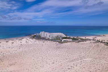 Dinamik hava görüntüleri Fuerteventura, Corralejo 'da lüks bir sahil oteli gösteriyor. Görüntü, beyaz kumlar, turkuaz sular ve modern mimari, seyahat, emlak ve yaşam tarzı fotoğrafçılığı arasındaki zıtlığı yakalıyor.. 