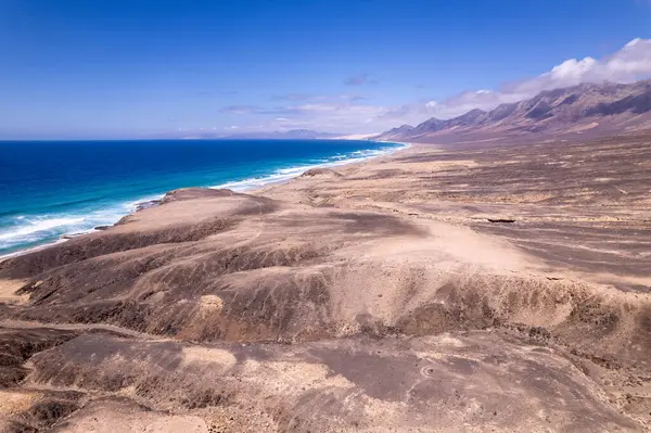 Muhteşem hava manzarası Fuerteventura 'daki Playa de Cofete' de Roque del Moro yakınlarında geniş bir sahili yakalıyor. Görüntü, seyahat fotoğrafçılığı için altın kumlar, turkuaz sular ve engebeli arazi arasındaki zıtlığı gösteriyor.. 