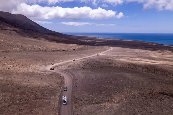 Dinamik hava görüntüleri, Fuerteventura, Jandia 'daki uzak okyanus yakınlarında dolambaçlı bir yol gösteriyor. Görüntü, turkuaz suların doğal güzelliği ile, seyahat ve yaşam tarzı fotoğrafçılığı arasındaki zıtlığı yakalıyor.. 